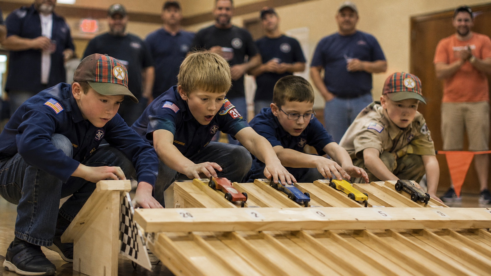 Boys leaning over the start gate of a wooden pinewood derby track